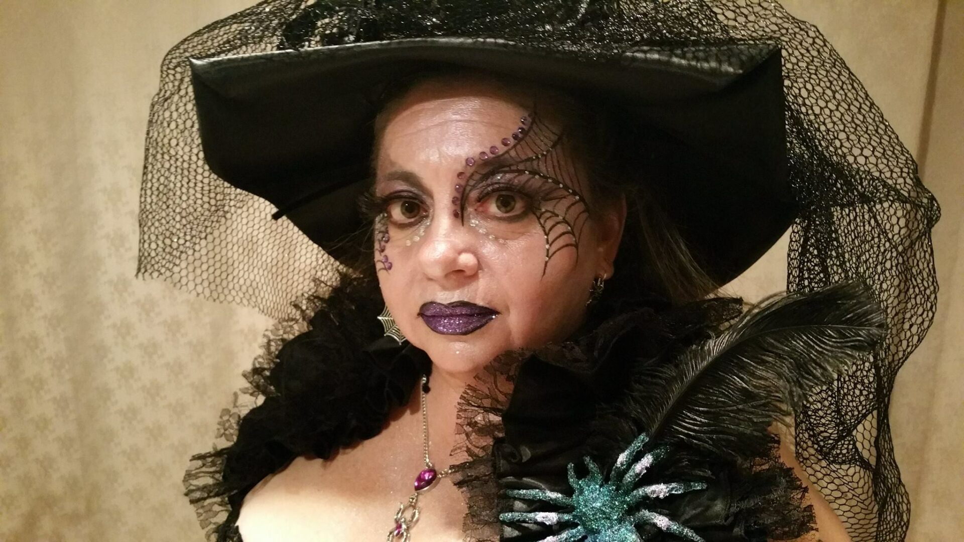 A woman in costume with spider and cobweb on her hat.