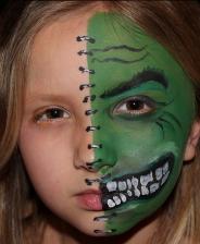 A girl with green face paint and teeth.