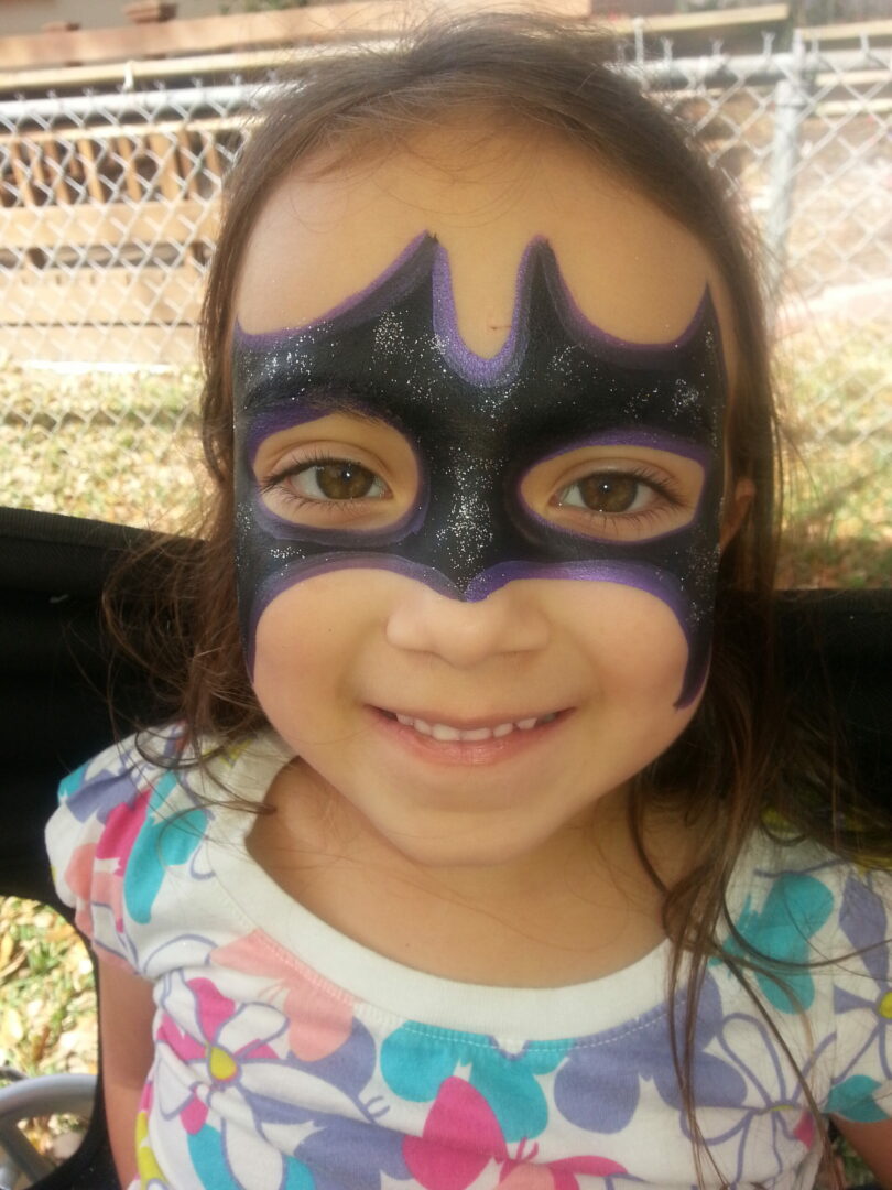 A little girl with a batman mask on her face.