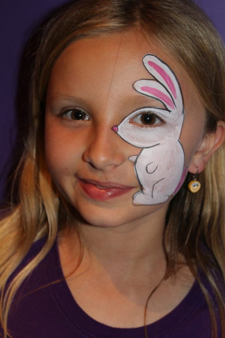 A girl with bunny face paint on her cheek.