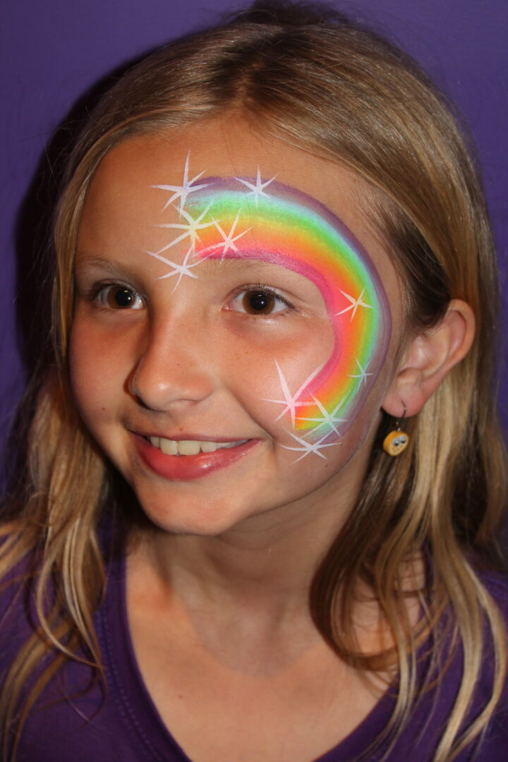 A girl with a rainbow face paint and earrings.