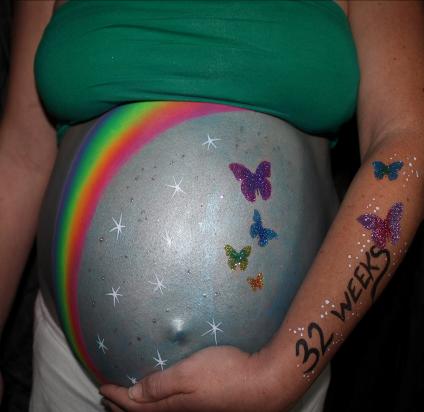 A pregnant woman holding her belly with butterflies and rainbow on it.